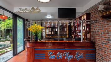 A bar area with a wooden counter, shelves with bottles, and a decorative hanging light fixture.