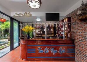 A bar area with a wooden counter, shelves with bottles, and a decorative hanging light fixture. - Tamcoc Ngoc Linh Homestay (Nam Hoa Lu)