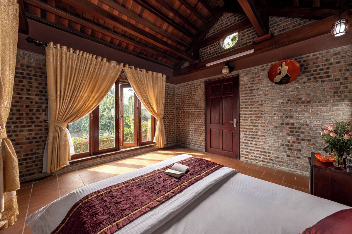 A room with a large bed, wooden beams, a brick wall, and a window with curtains.