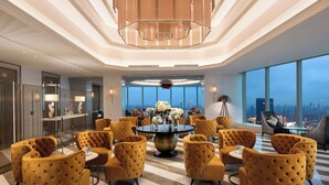 Eine großzügige Lobby mit einem runden Tisch in der Mitte, umgeben von gelben, gepolsterten Stühlen, großen Fenstern mit Blick auf die Stadt und einer modernen Chandelier.