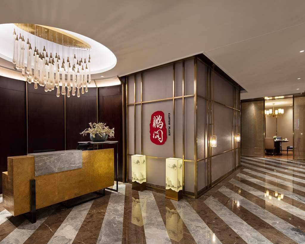 Un moderno vestíbulo de hotel con una recepción, una lámpara decorativa y un símbolo chino tradicional en la pared.