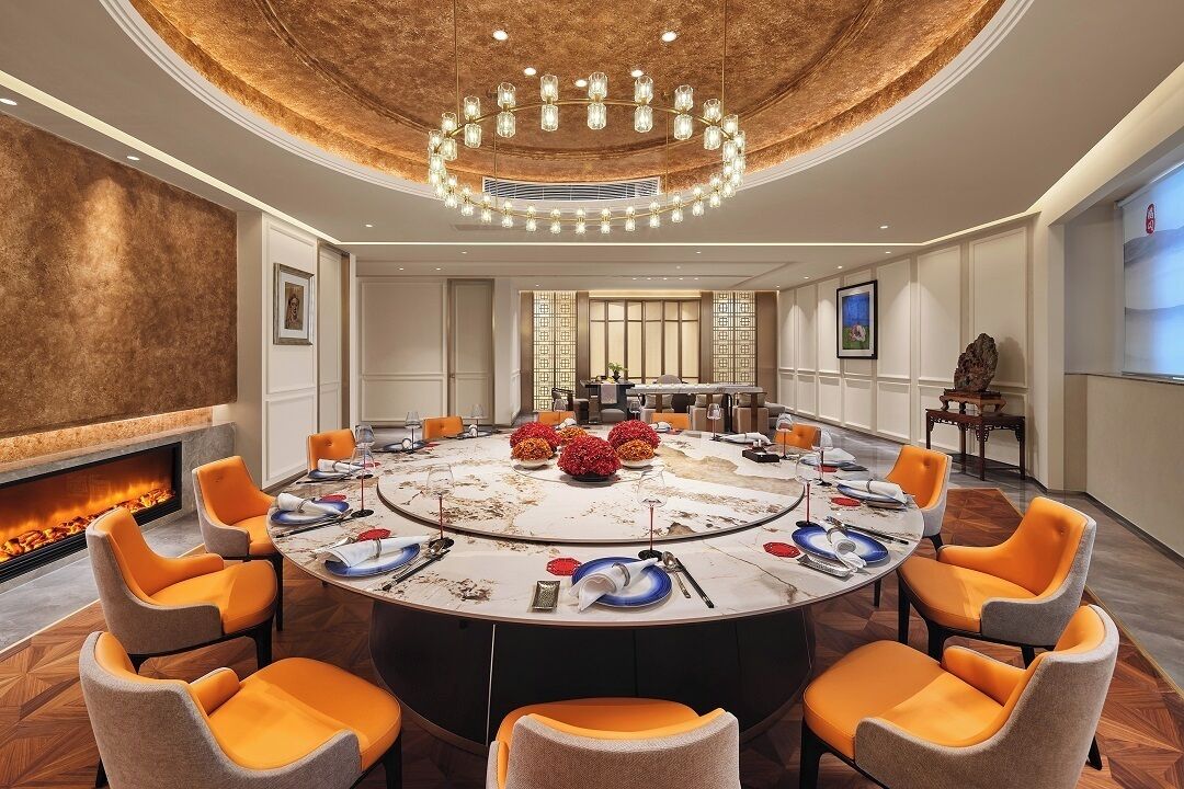 A conference room with a round table, orange chairs, a fireplace, and a chandelier.