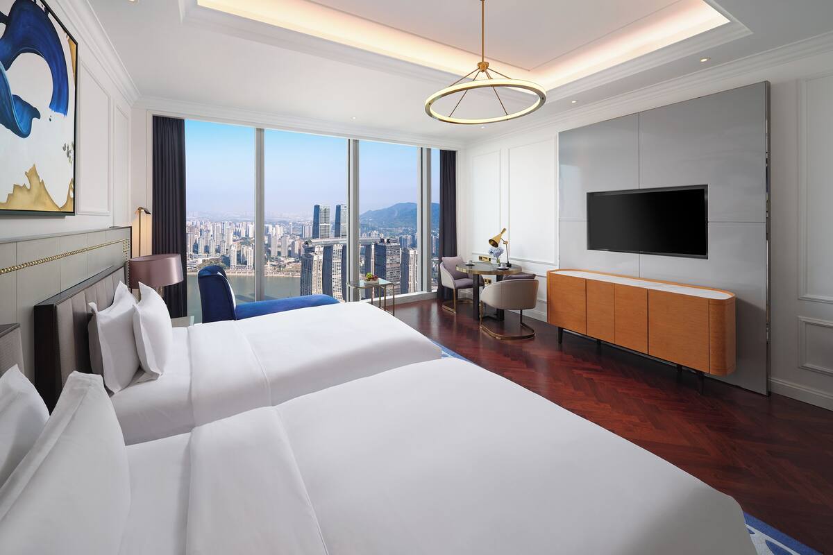 A hotel room with a large bed, a desk, a chair, a TV, and a city view.