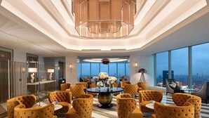 Eine geräumige Lobby mit einem runden Tisch in der Mitte, umgeben von gelben Polstersesseln, einer modernen Kronleuchter und großen Fenstern mit Blick auf die Stadt.
