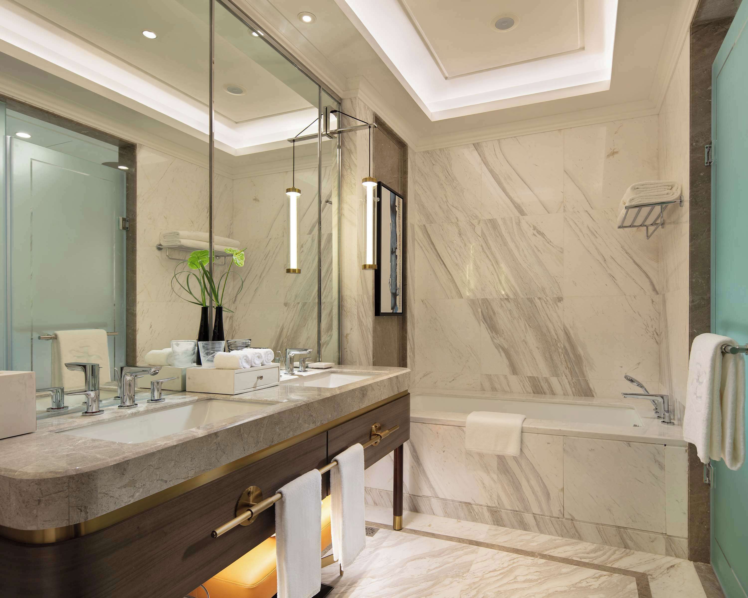 A modern bathroom with a large mirror, dual sinks, a bathtub, and marble walls.