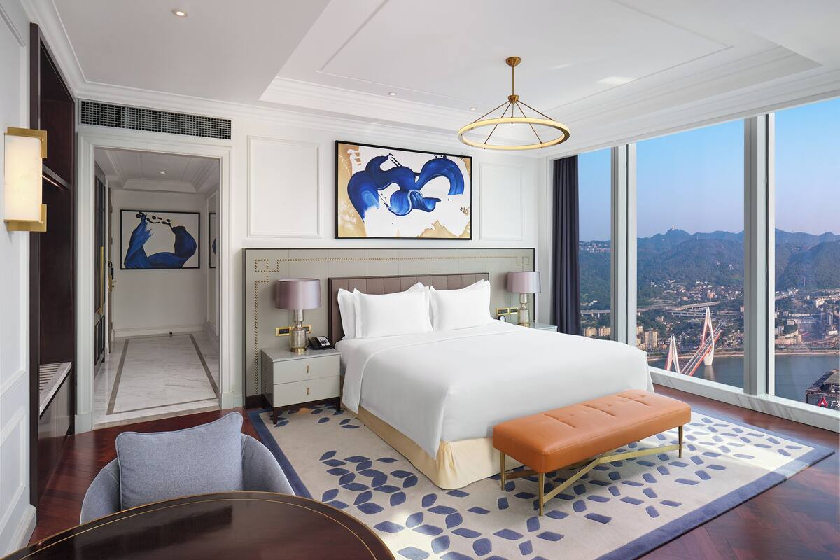 A spacious hotel room with a large bed, a view of a cityscape, and a modern design.