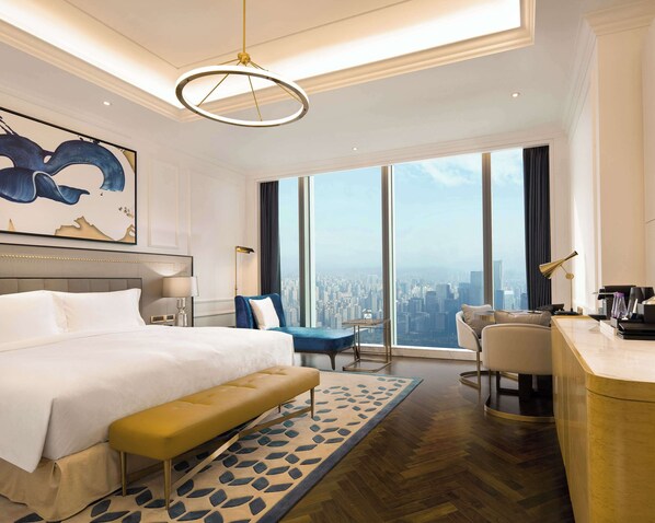 A modern hotel room with a large bed, a desk, a chair, and a view of the city.