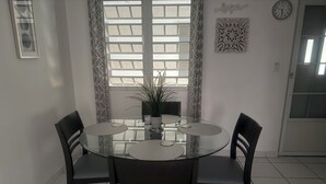 Un comedor con una mesa de vidrio rodeada por cuatro sillas, una planta en maceta y un reloj en la pared.