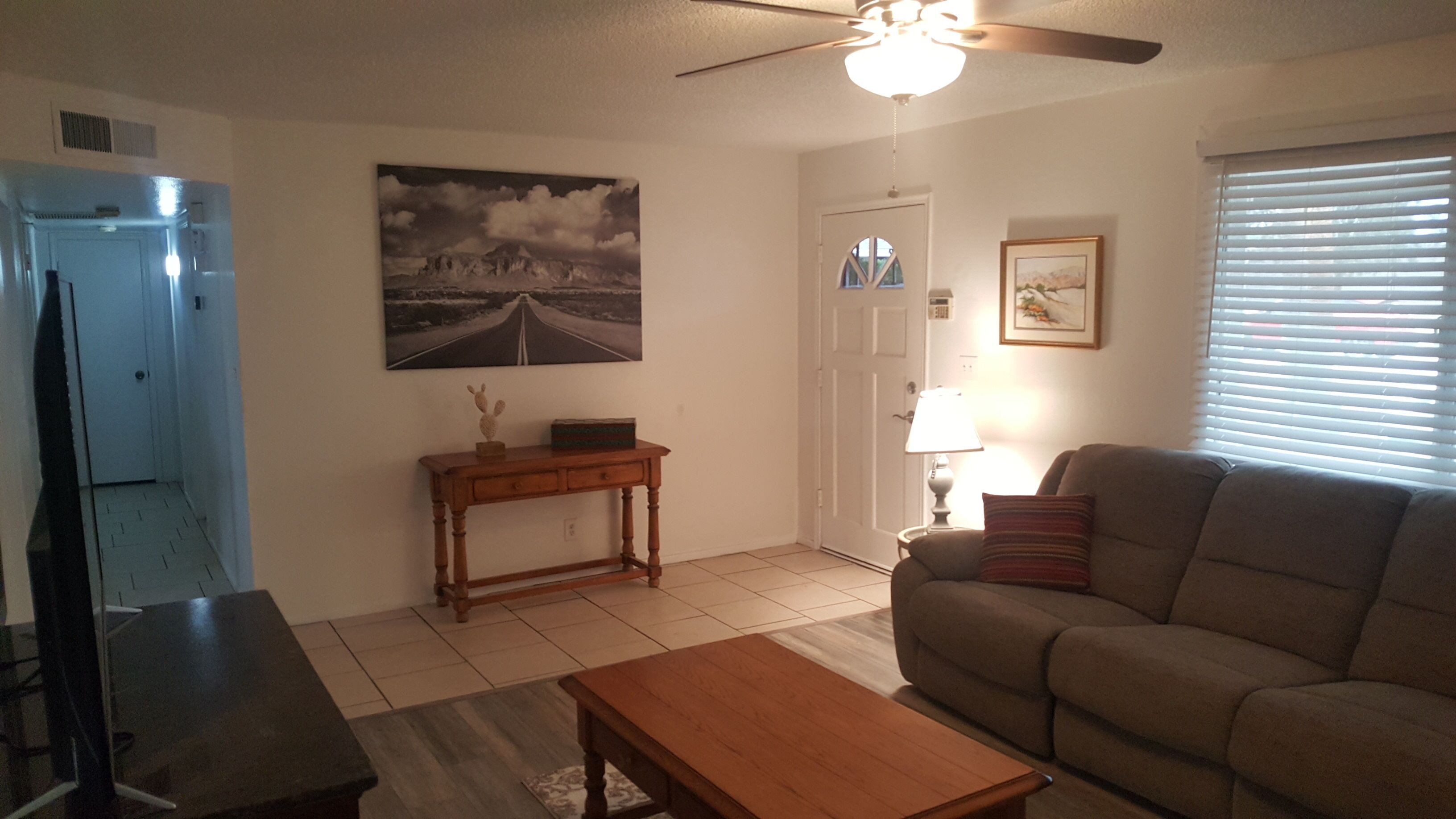 A living room with a sofa, a coffee table, a TV, a ceiling fan, and a painting on the wall.
