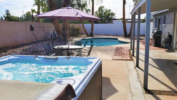 Un jardin avec un jacuzzi, une piscine, du mobilier de jardin et un espace couvert.
