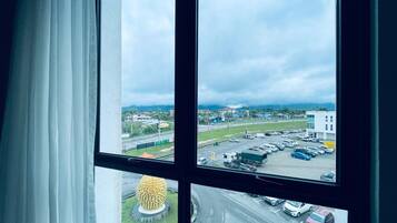 Vista desde una ventana con cortinas blancas, que da a un estacionamiento con varios coches y un edificio al fondo.