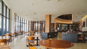 Ein geräumiges Café mit Holztischen und -stühlen, großen Fenstern und einer gewölbten Theke.