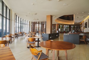 Um café espaçoso com mesas e cadeiras de madeira, grandes janelas e um balcão curvo.