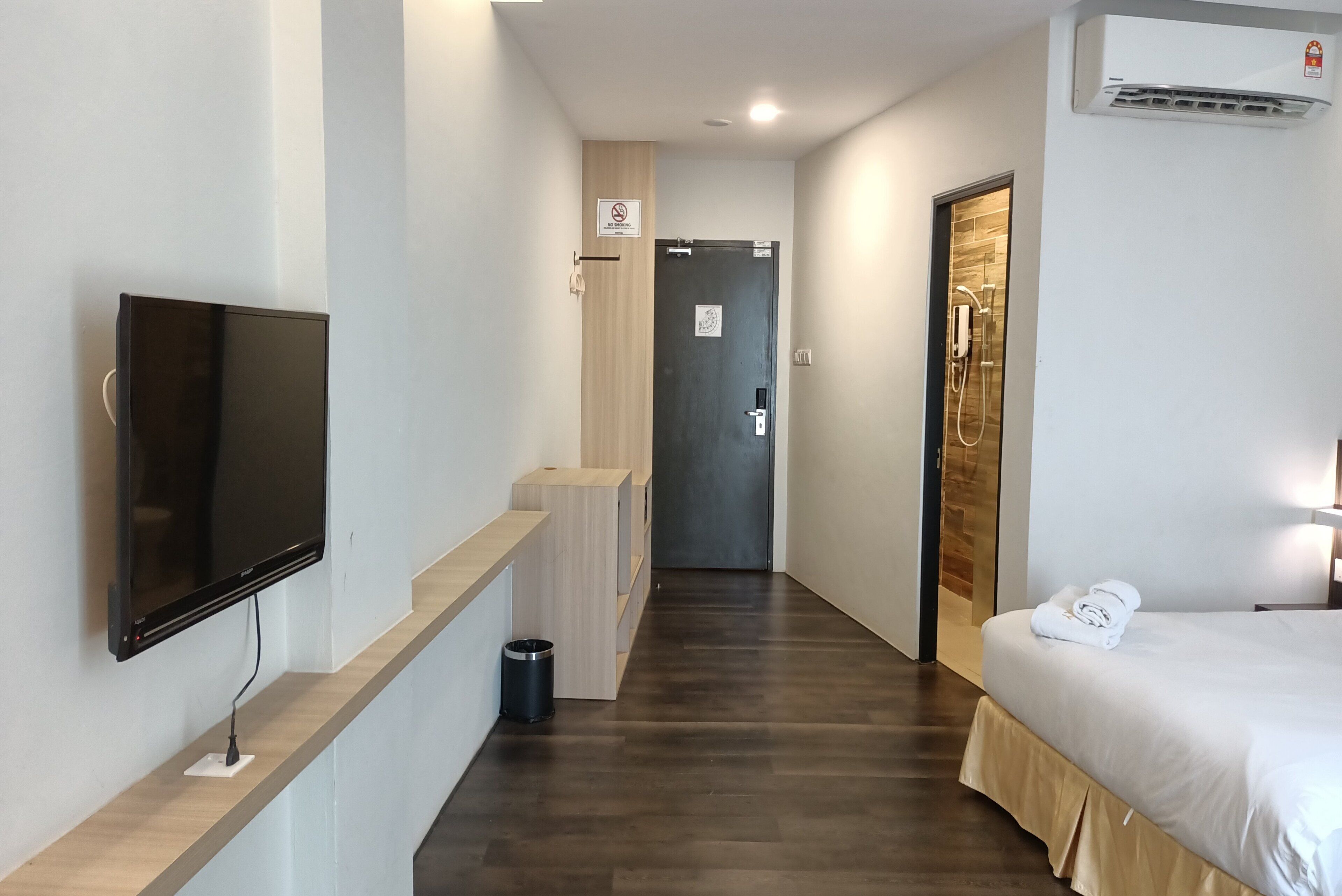 Ett hotellrum med en säng, en tv, en dusch och en hall som leder till en dörr.