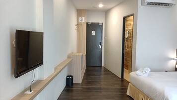 Ett hotellrum med en säng, en tv, en dusch och en hall som leder till en dörr.