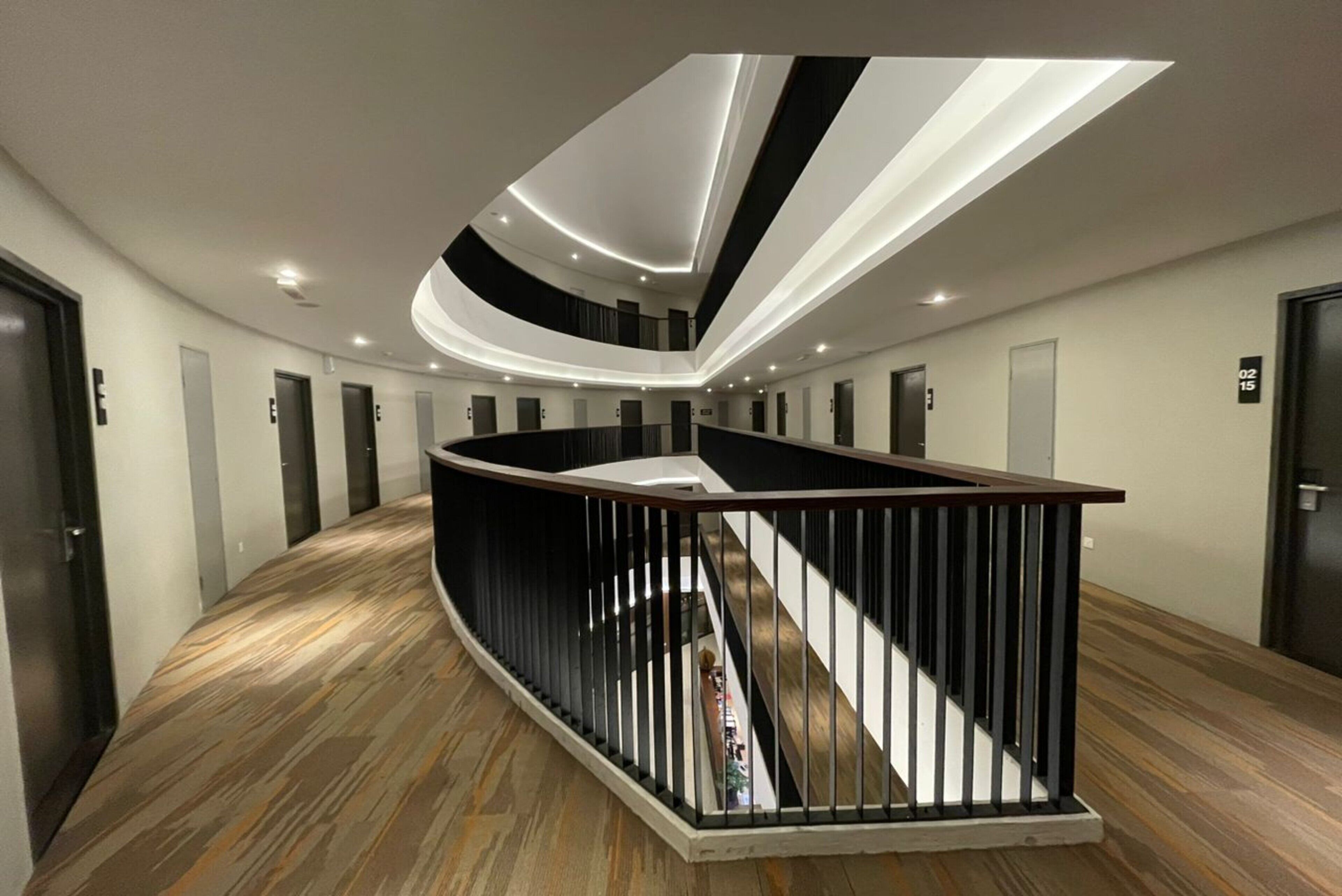 A modern hotel lobby with a curved staircase, recessed lighting, and a central island.