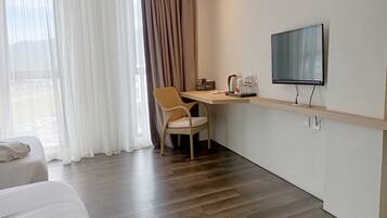 Habitación de hotel con cama, escritorio con silla, televisión y ventana con cortinas.