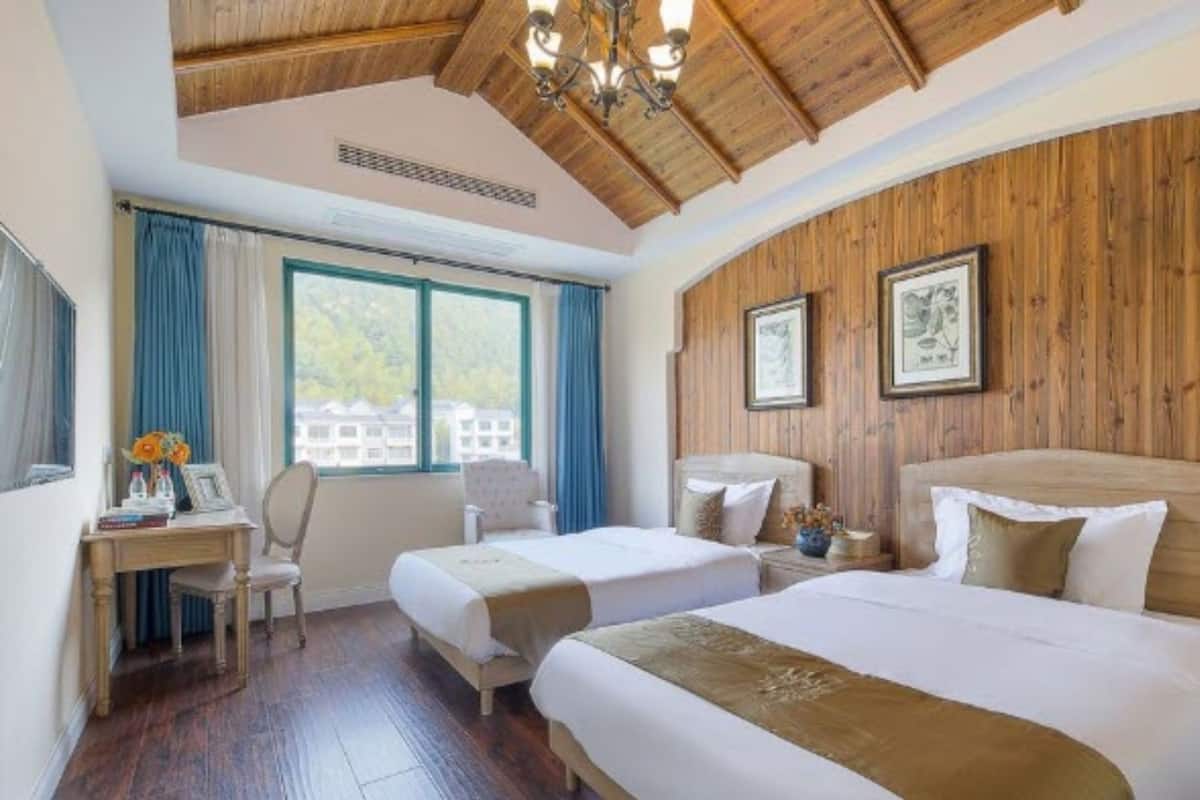 Habitación de hotel con dos camas, paneles de madera en las paredes, un escritorio con silla y una ventana con cortinas.