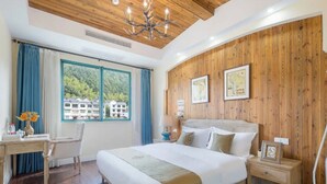 Une chambre d’hôtel avec un grand lit, des murs lambrissés, un bureau avec une chaise, une table de chevet et une vue sur les bâtiments par la fenêtre.