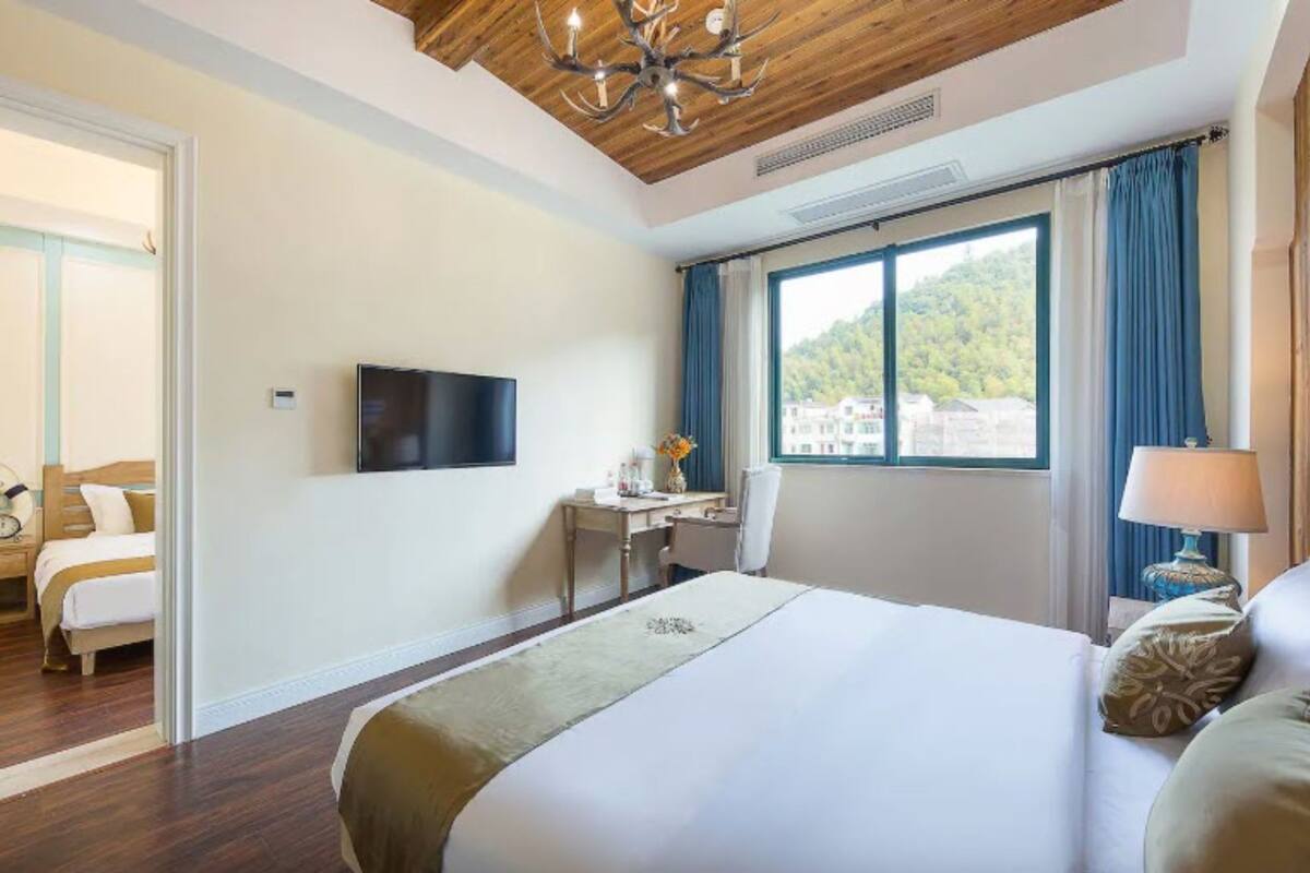 Habitación de hotel con una cama grande, un escritorio, una silla, un televisor y una ventana con vistas a edificios y árboles.