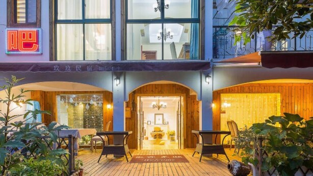 L’entrée d’un hôtel, avec une façade en bois, un panneau lumineux et un espace extérieur accueillant avec des sièges.