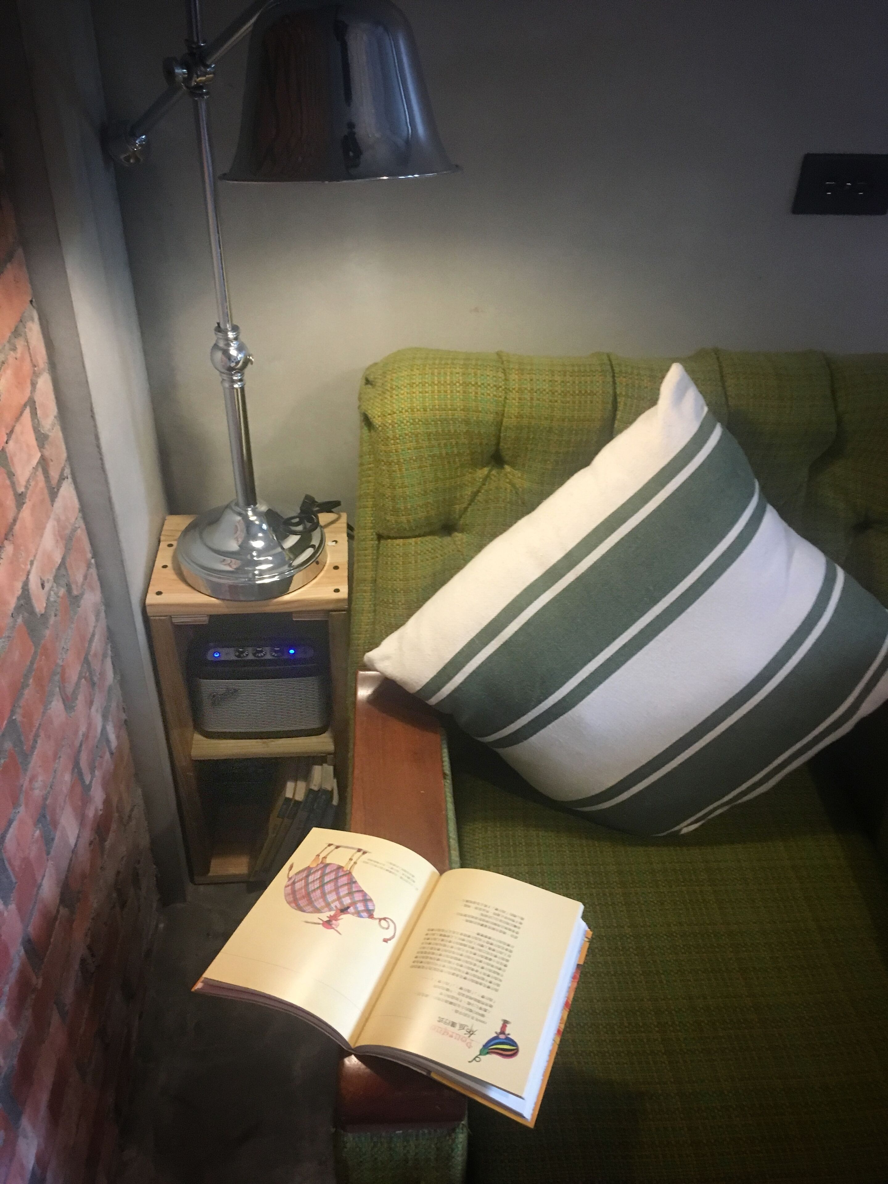 Un rincón acogedor para leer con un sofá verde, un cojín a rayas, una lámpara y un libro.