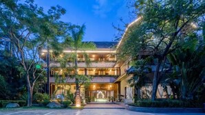 A multi-story hotel with a central entrance, surrounded by lush greenery and palm trees. - Floral Hotel · River Rhythms Pavilion Jinghong (Xishuangbanna Dai)