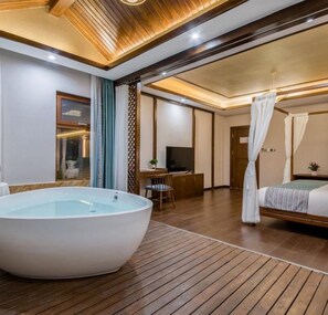 A modern hotel room with a large bathtub, a desk with a computer, and a bed with a canopy. - Floral Hotel · River Rhythms Pavilion Jinghong (Xishuangbanna Dai)
