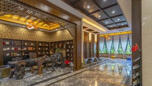 A lobby with a marble floor, wooden furniture, and shelves with decorative items. - Floral Hotel · River Rhythms Pavilion Jinghong (Xishuangbanna Dai)