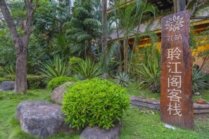 Une enseigne en bois ornée de caractères chinois, entourée d’une végétation luxuriante et de gros rochers.