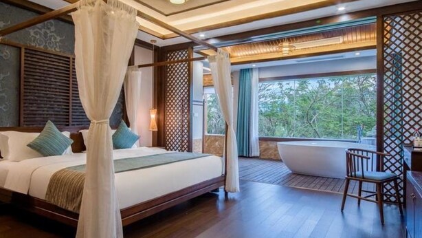 A bedroom with a large bed, a canopy, a view of the outdoors, a bathtub, and a wooden floor. - Floral Hotel · River Rhythms Pavilion Jinghong (Xishuangbanna Dai)