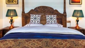 Un lit à baldaquin avec une tête de lit en bois foncé, deux lampes assorties de chaque côté et des coussins décoratifs à motifs.