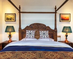 A four-poster bed with a dark wooden headboard, two matching lamps on either side, and patterned throw pillows.