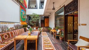 A courtyard with a long wooden bench, a table, and chairs. There are potted plants and a staircase leading to an upper level.