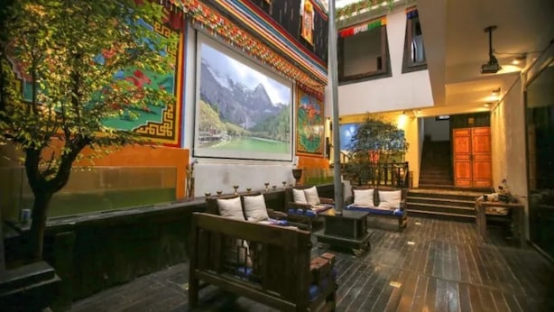 An indoor seating area with wooden benches and cushions, a mural of a mountain landscape, and a staircase leading to an upper level.