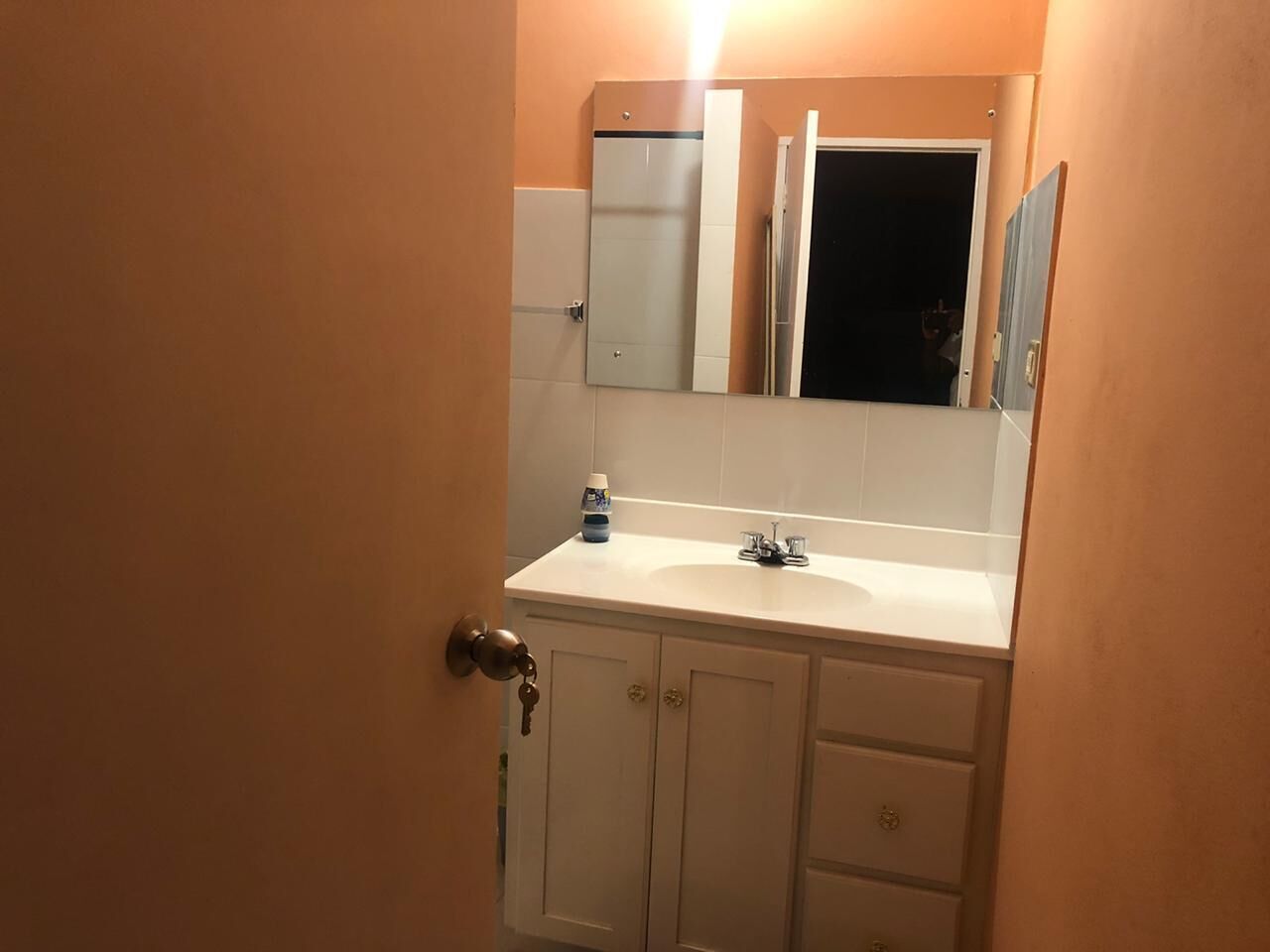 A bathroom with a white sink, mirror, and cabinets.