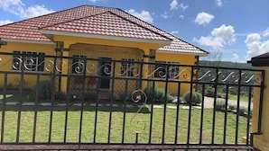 Een geel huis met een rode dakbedekking en een zwarte metalen hek voor.