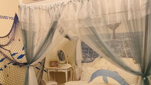 A bedroom with a bed covered by a sheer canopy, a bedside table with a mirror, and a wall with a decorative fish net. - Nasun bed and breakfast (Jianshi)