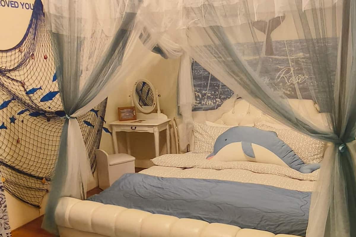 A bedroom with a bed covered by a sheer canopy, a bedside table with a mirror, and a wall with a decorative fish net.