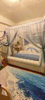 A bedroom with a bed covered by a sheer canopy, a bedside table with a mirror, and a wall with a decorative fish net.