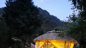 A thatched-roof outdoor seating area with stone steps leading up to it, surrounded by greenery and a mountain in the background. - Nasun bed and breakfast (Jianshi)