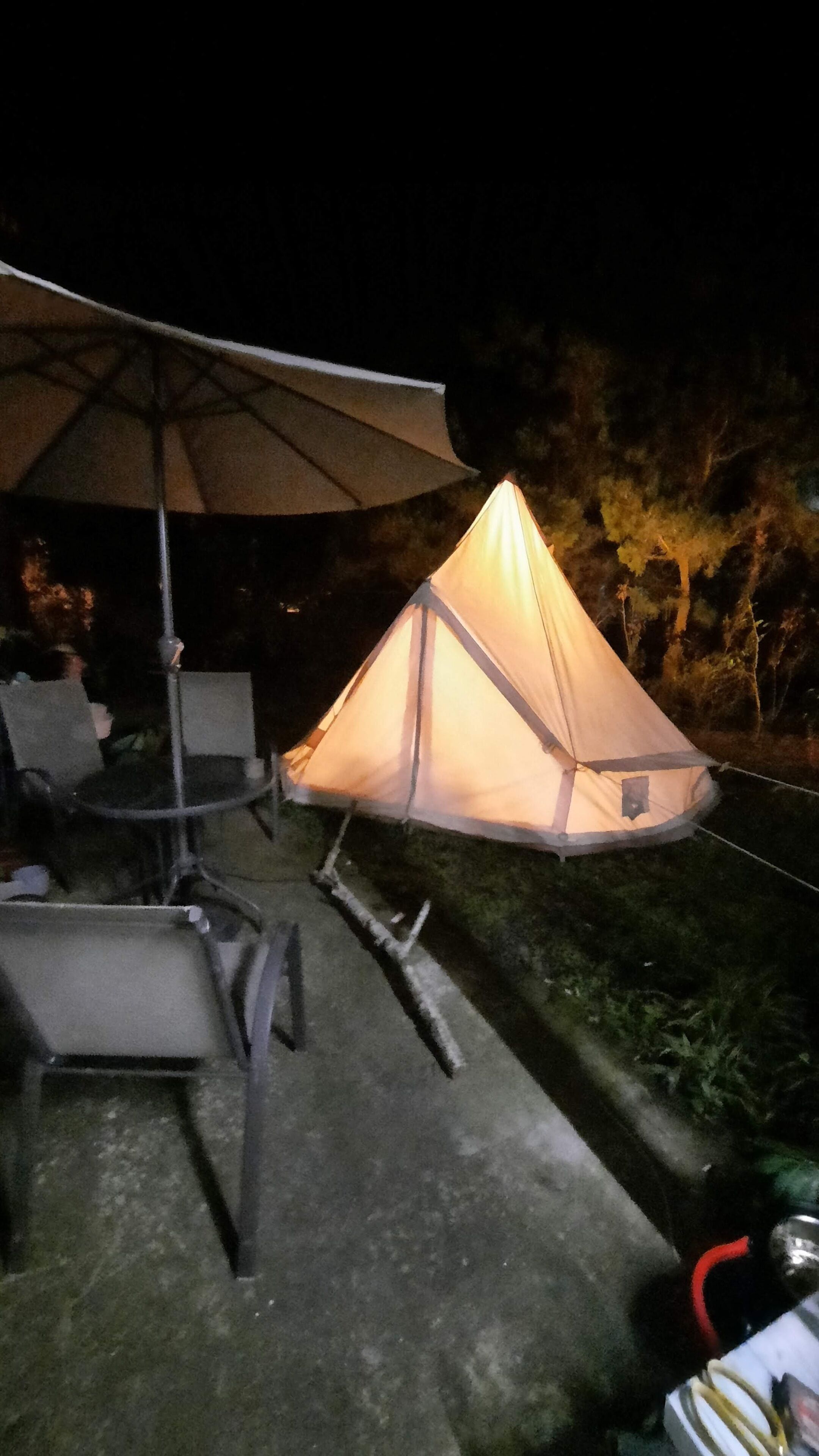 A tent with a canopy, surrounded by chairs and a table, set up outdoors at night.