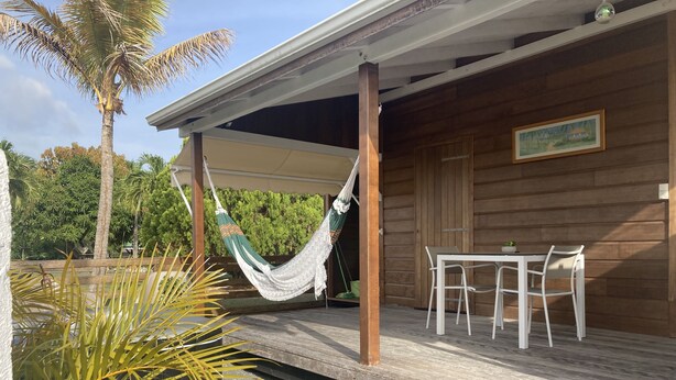 Een houten gebouw met een overdekte veranda, een hangmat, een tafel met stoelen en een schilderij aan de muur.