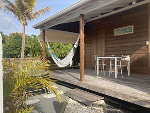 A wooden building with a covered porch, a hammock, a table with chairs, and a painting on the wall. - EXOTIC WOODEN BUNGALOW IN THE COUNTRY (PETIT - CANAL)