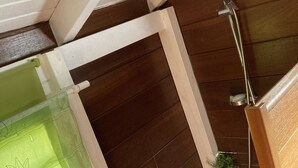 Een hoek van een kamer met houten wanden, een douchegedeelte en een groen gordijn met bladmotief.