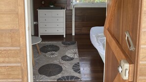 Een kleine slaapkamer met houten vloer, een bed, een nachtkastje met lamp en een klein dressoir.