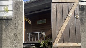 Een houten schuurtje in rustieke stijl met een openstaande deur, waarachter een klein zitgedeelte met een tafel en stoelen zichtbaar is.