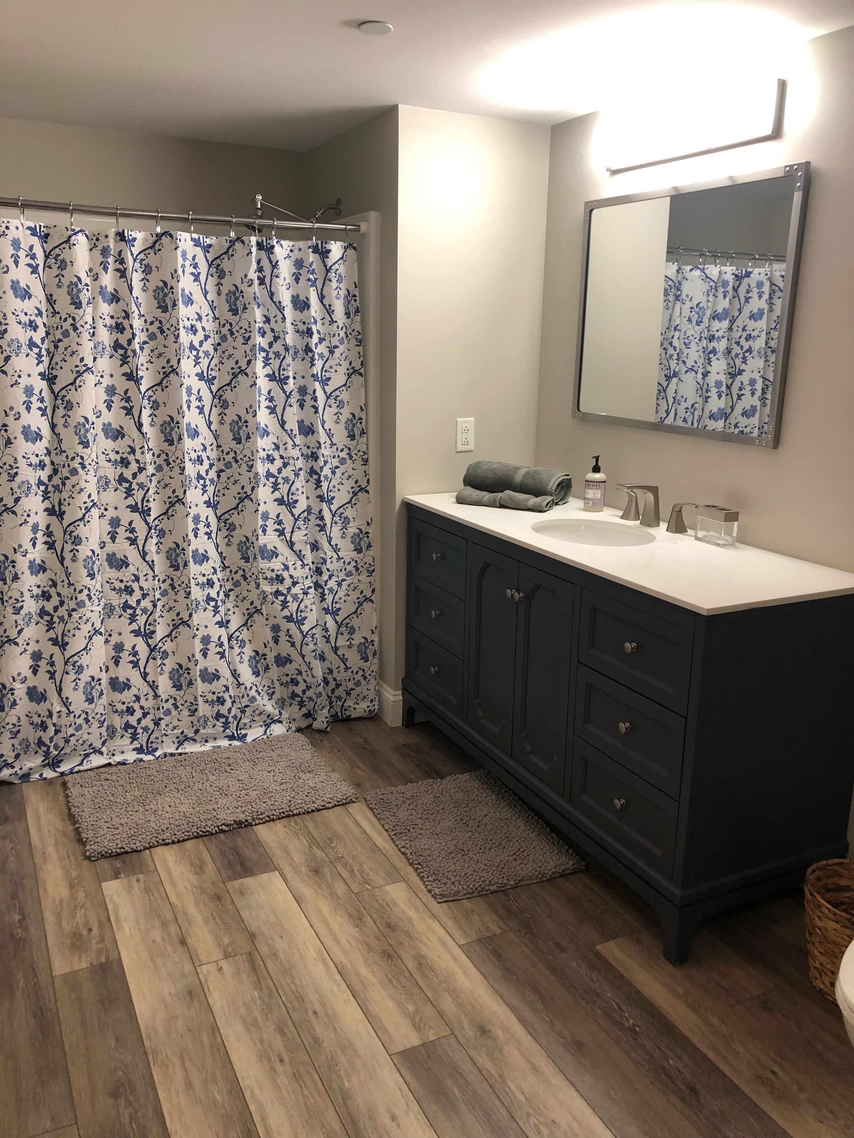 A bathroom with a shower curtain, a sink, a mirror, and a wooden floor.