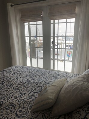 Ein Bett mit einem gemusterten Überwurf und zwei Kissen, ein Fenster mit weißen Vorhängen und im Hintergrund eine Aussicht auf ein Riesenrad und einen Vergnügungspark.
