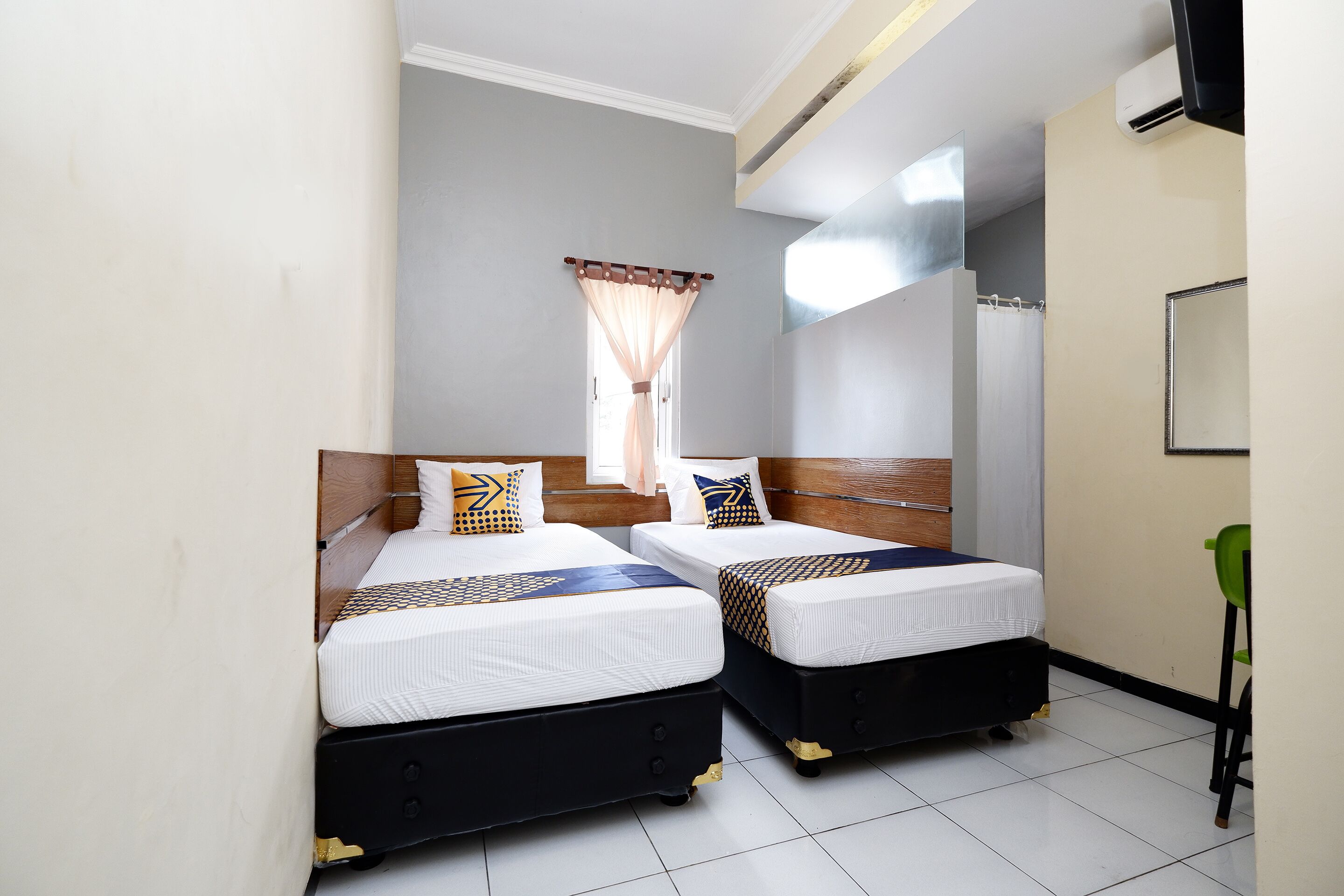 Une chambre d’hôtel avec deux lits, une fenêtre avec des rideaux, un miroir et une chaise verte.